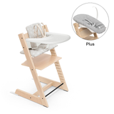 The image shows a Tripp Trapp highchair with a white seat and natural wood frame, accompanied by a newborn set with a Stokke starry cushion and a Stokke tray.